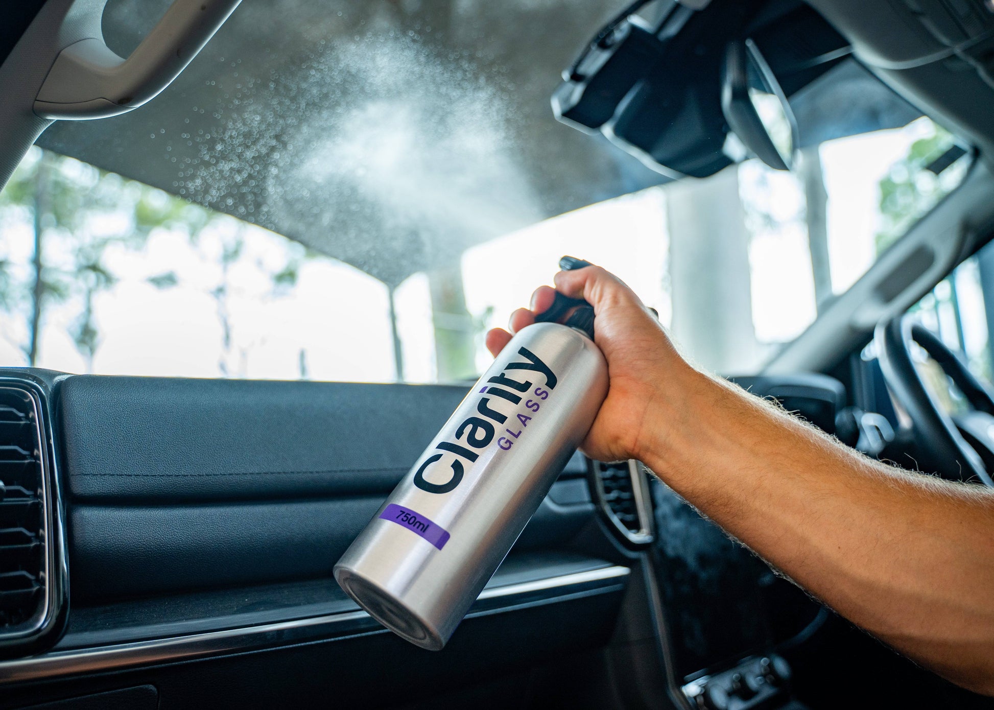 Clarity Glass Cleaner spraying interior windshield - ammonia-free formula removes haze, fingerprints, and streaks for perfect visibility while driving.