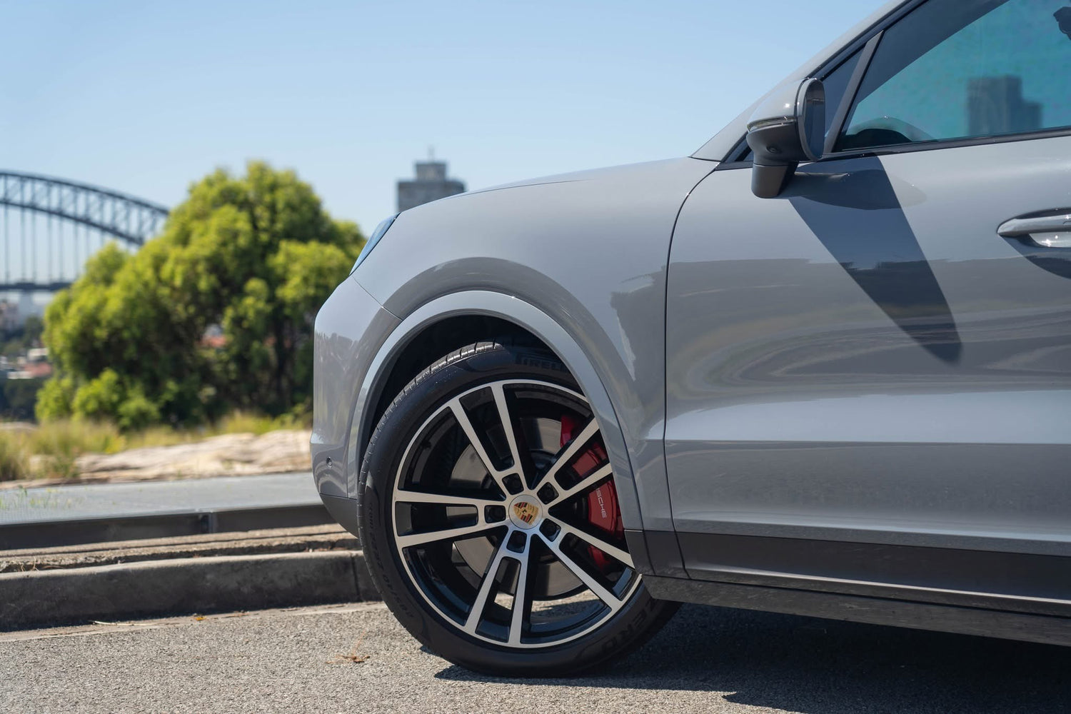 Gray car with black rim on a road with trees and bridge in the background
