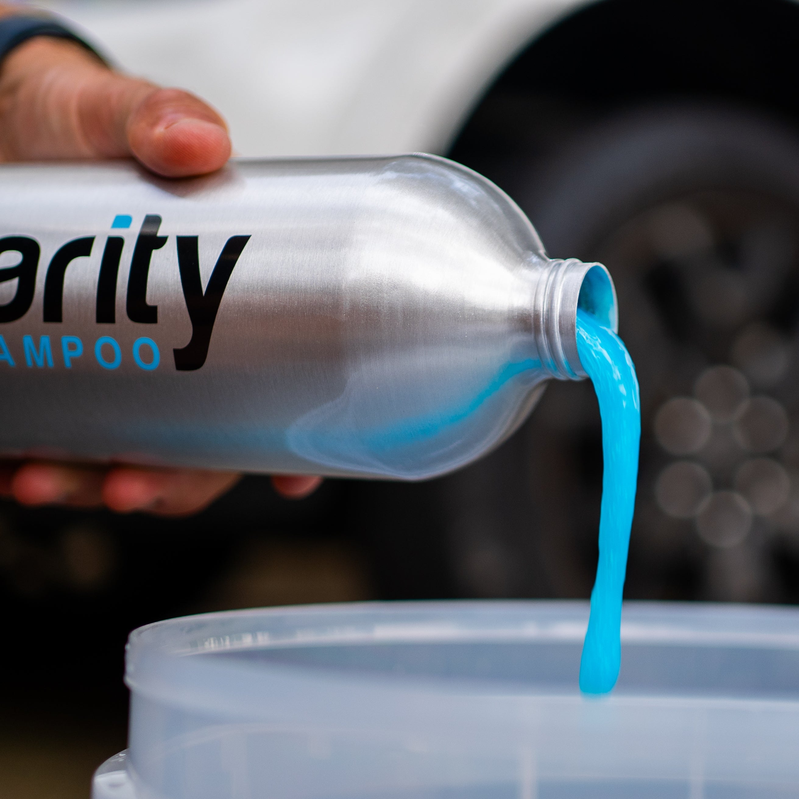 Person pouring a blue liquid from a bottle labeled 'variety shampoo' into a container with a car in the background.