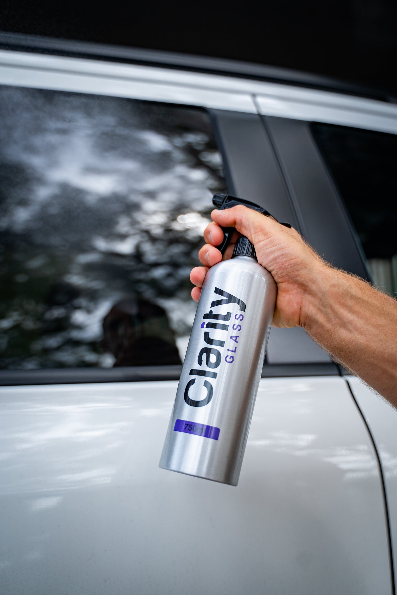 Person holding a Clarity Glass cleaner can in front of a car window.