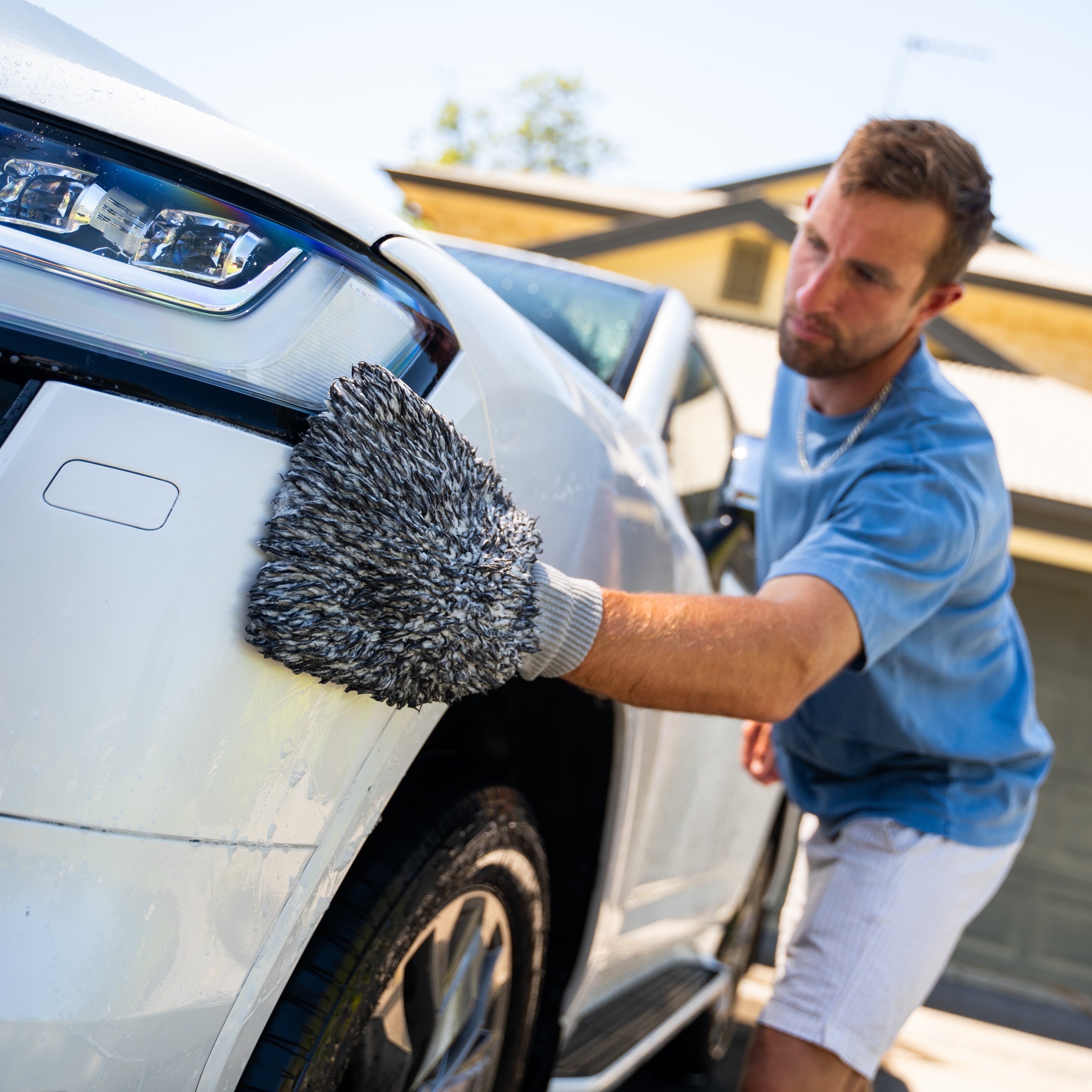 Man cleaning a white car with a gray microfiber cloth in front of a house.