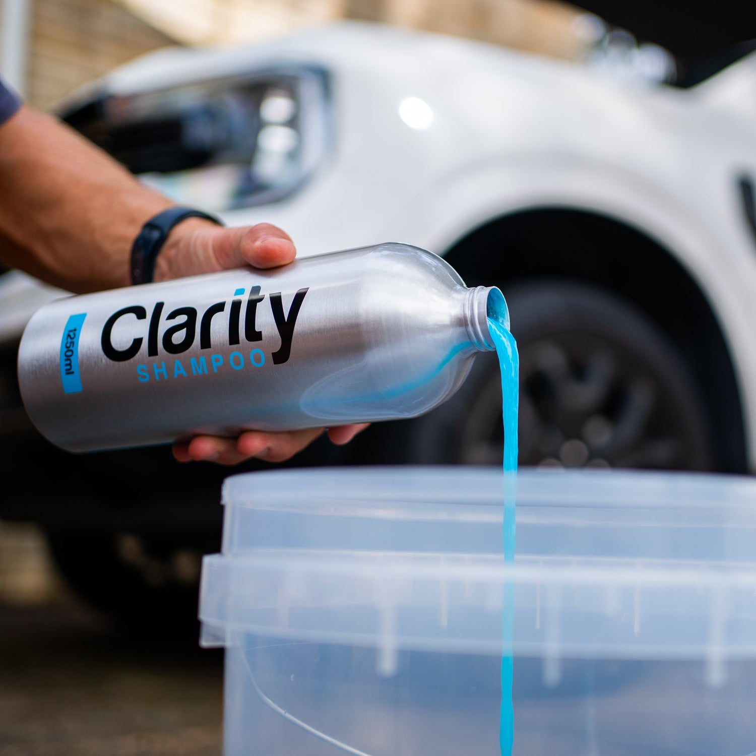 Person pouring Clarity shampoo into a container with a car in the background